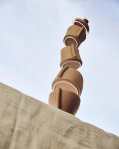 Gatherware stackable clay cups balanced in a tall terracotta stack against a pale sky, above a linen-covered ledge, by Boo Design Studio