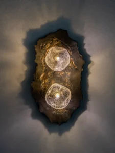Asea No. 25 wall sconce with two glowing hand-blown glass globes set in a wavy dark stoneware plate by Ceren Gürkan