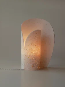 Kalia table lamp in translucent bone-white resin with embedded glass particles, glowing warm amber, by Justyna Poplawska